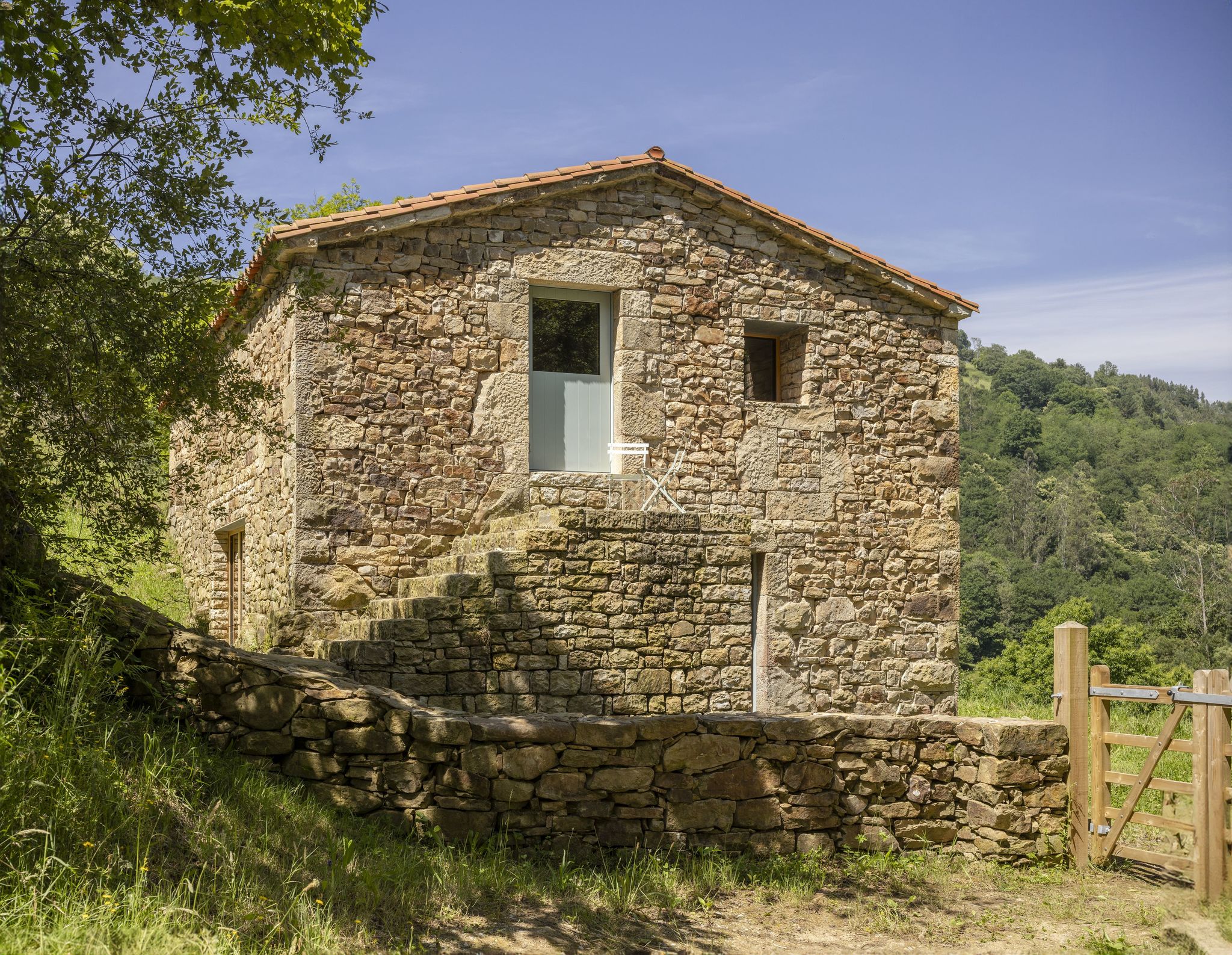 La rehabilitación respeta la volumetría original, los muros de piedra de hasta 80 cm de espesor, la cubierta inclinada y la escalera de piedra exterior característica de esta tipología vernácula.